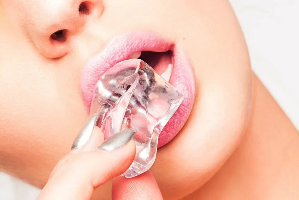 Close-up of lips with pink lipstick holding an ice cube, hand with metallic silver nails