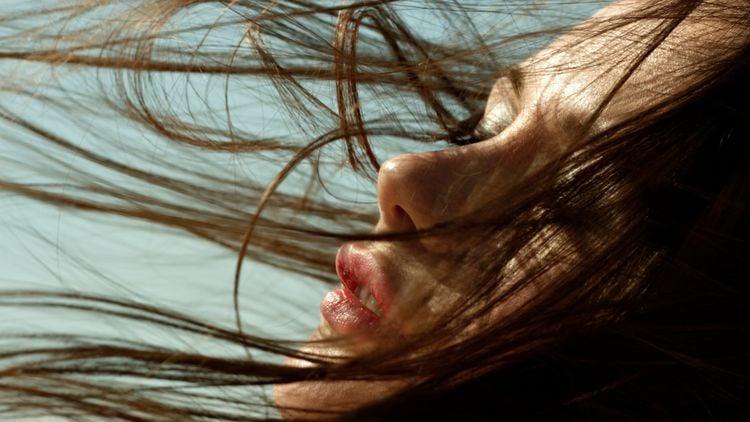 Close-up of a woman's face with flowing hair in natural light against a clear sky background