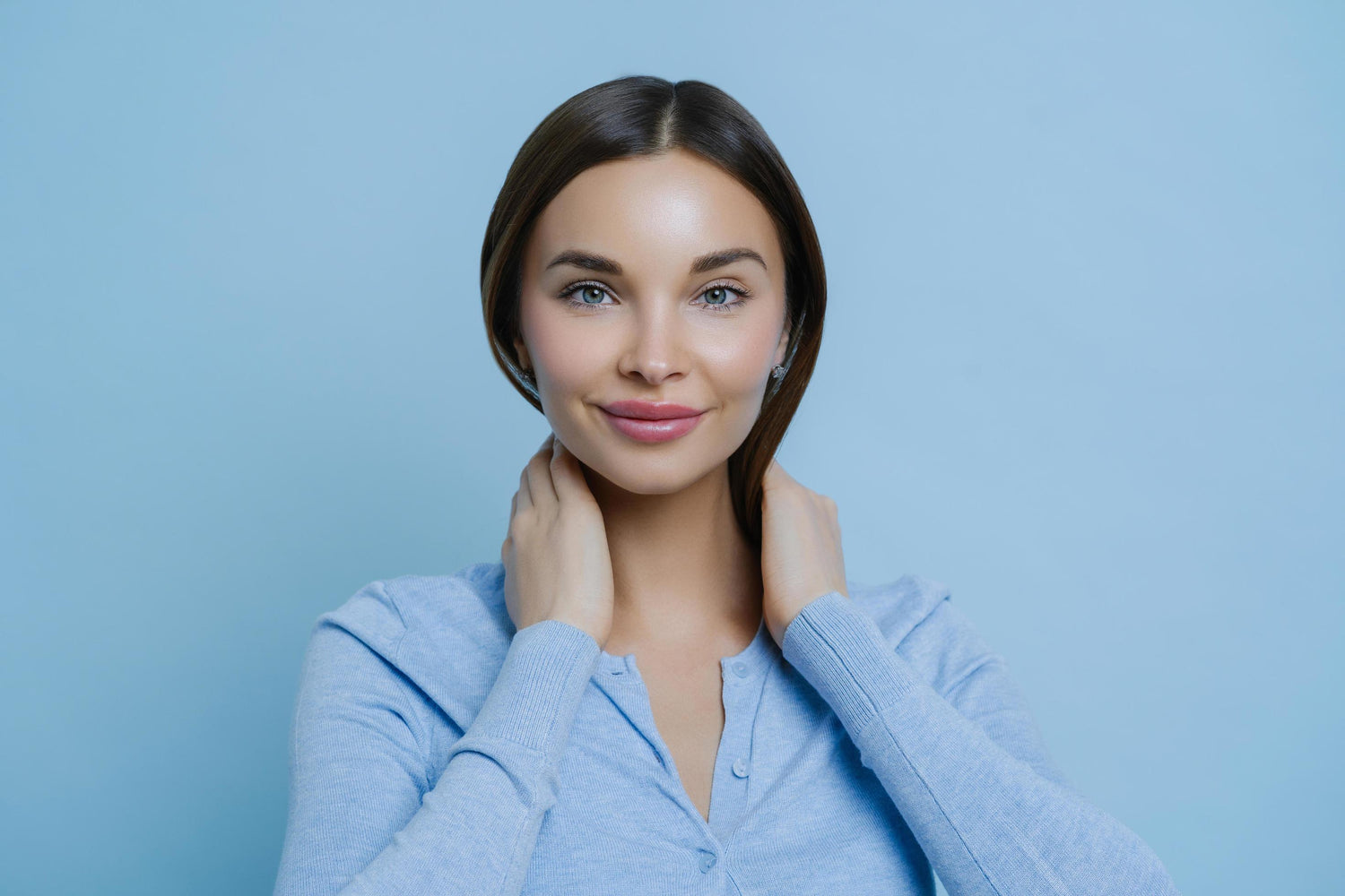 Portrait of a smiling woman with blue eyes and brown hair wearing a light blue cardigan against a blue background