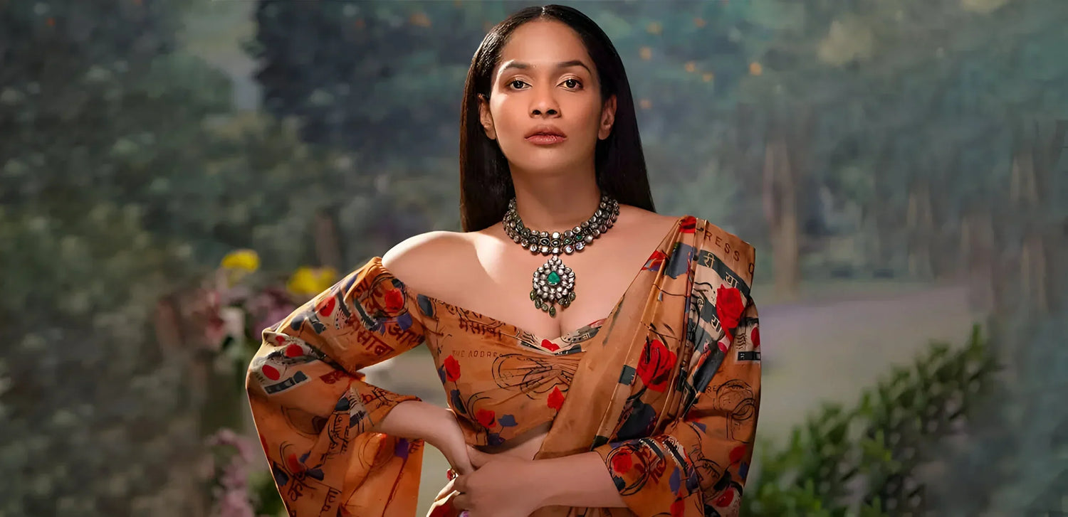 Woman in orange floral saree with statement necklace posing outdoors with blurred green background