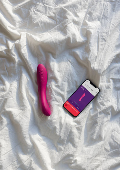 Roze vibrerende stimulator op bed met smartphone en productkaart