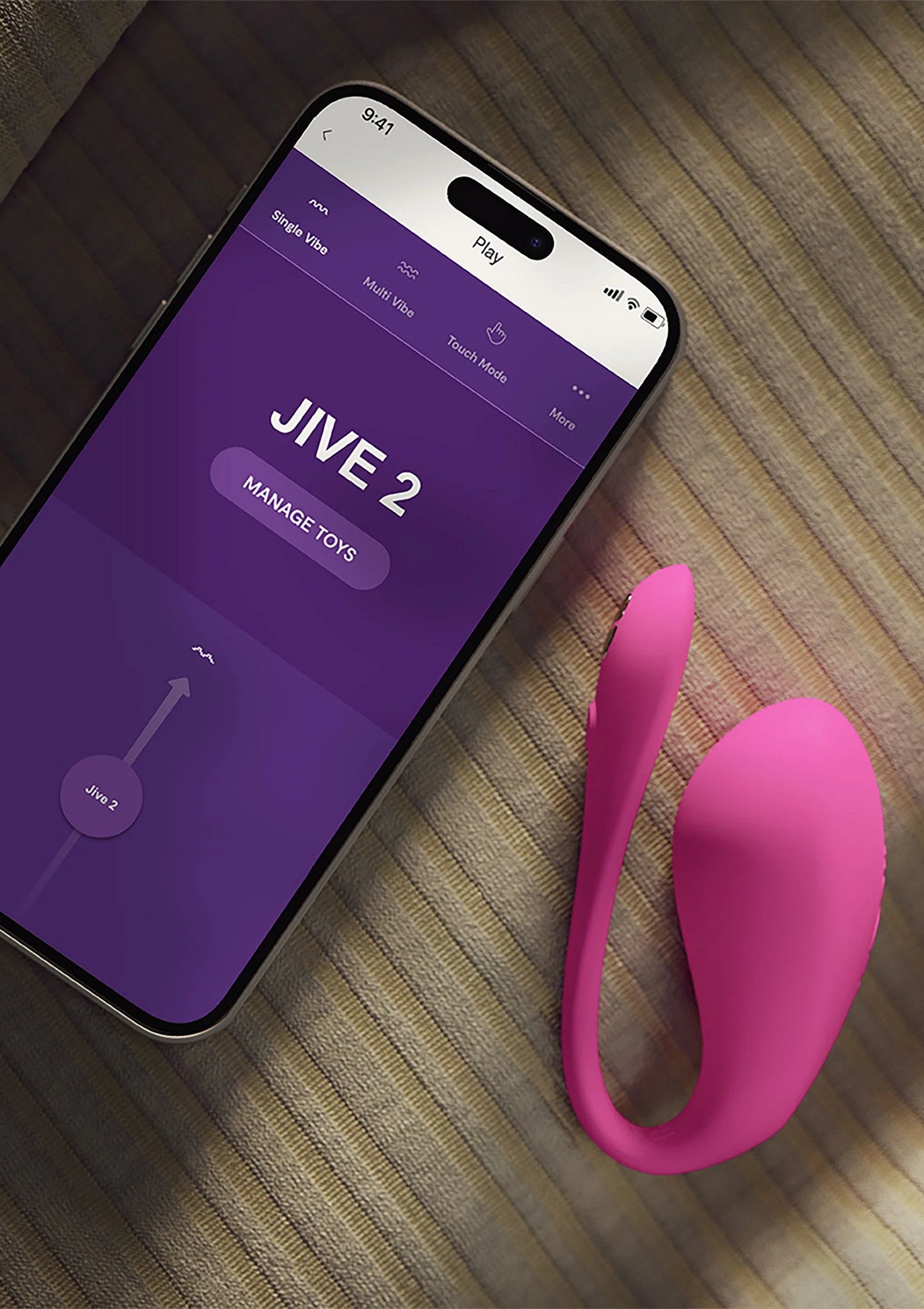 We-Vibe Jive 2 duo-vibrator in felroze naast smartphone met paarse app-interface