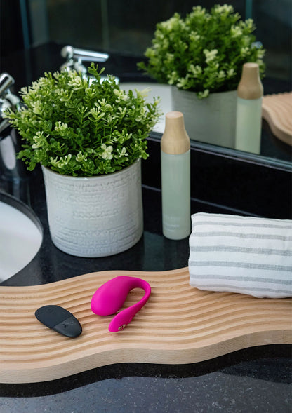 We-Vibe Jive 2 duo-vibrator in felroze op een houten plank met zwarte afstandsbediening