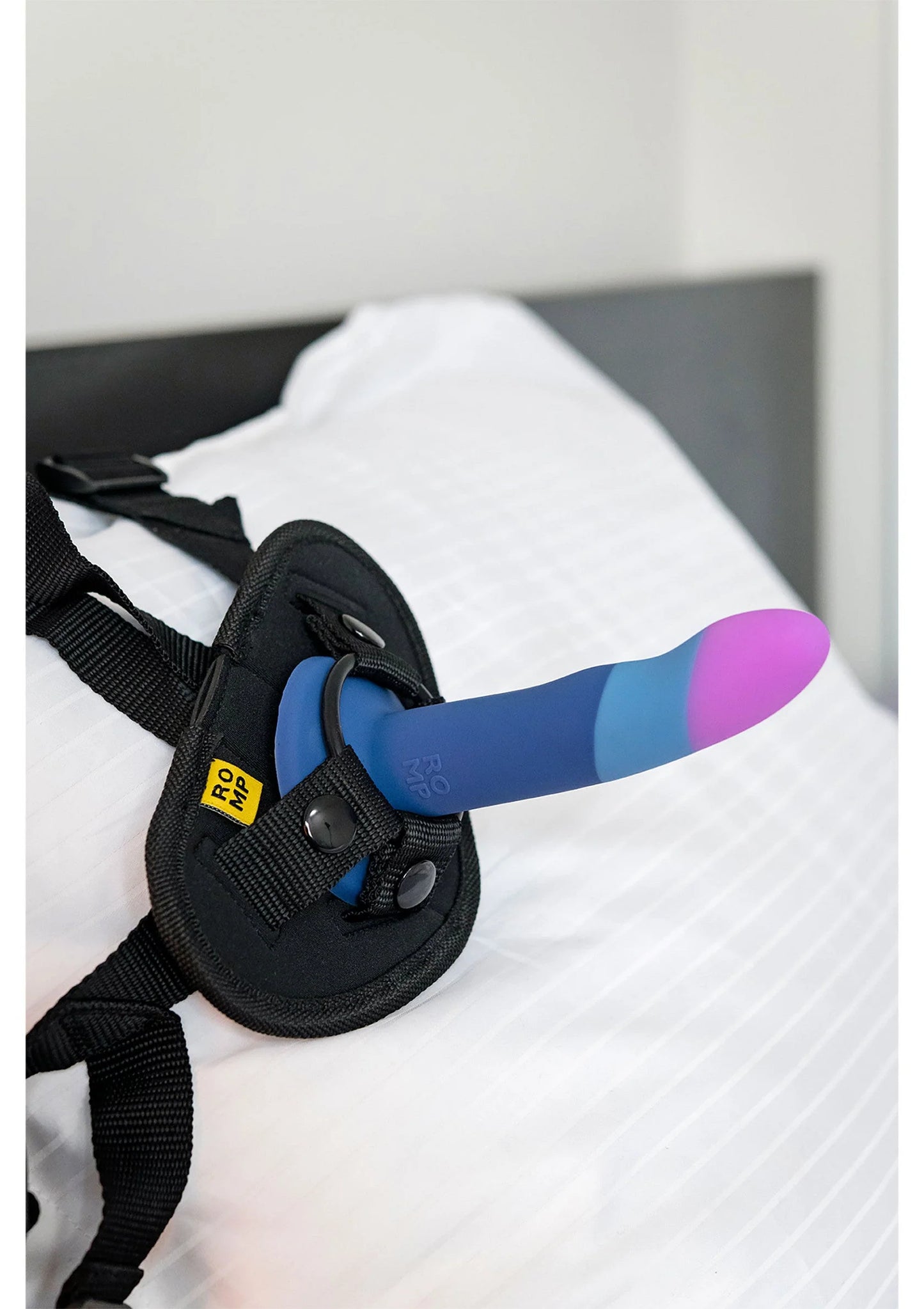 Zwarte draagriem met blauwe–paarse dildo op wit textiel