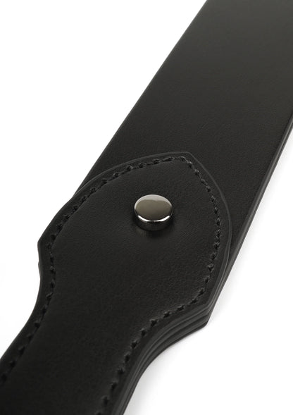 Detail van zwarte leren slapper: ronde metalen drukknop op afgeronde flap
