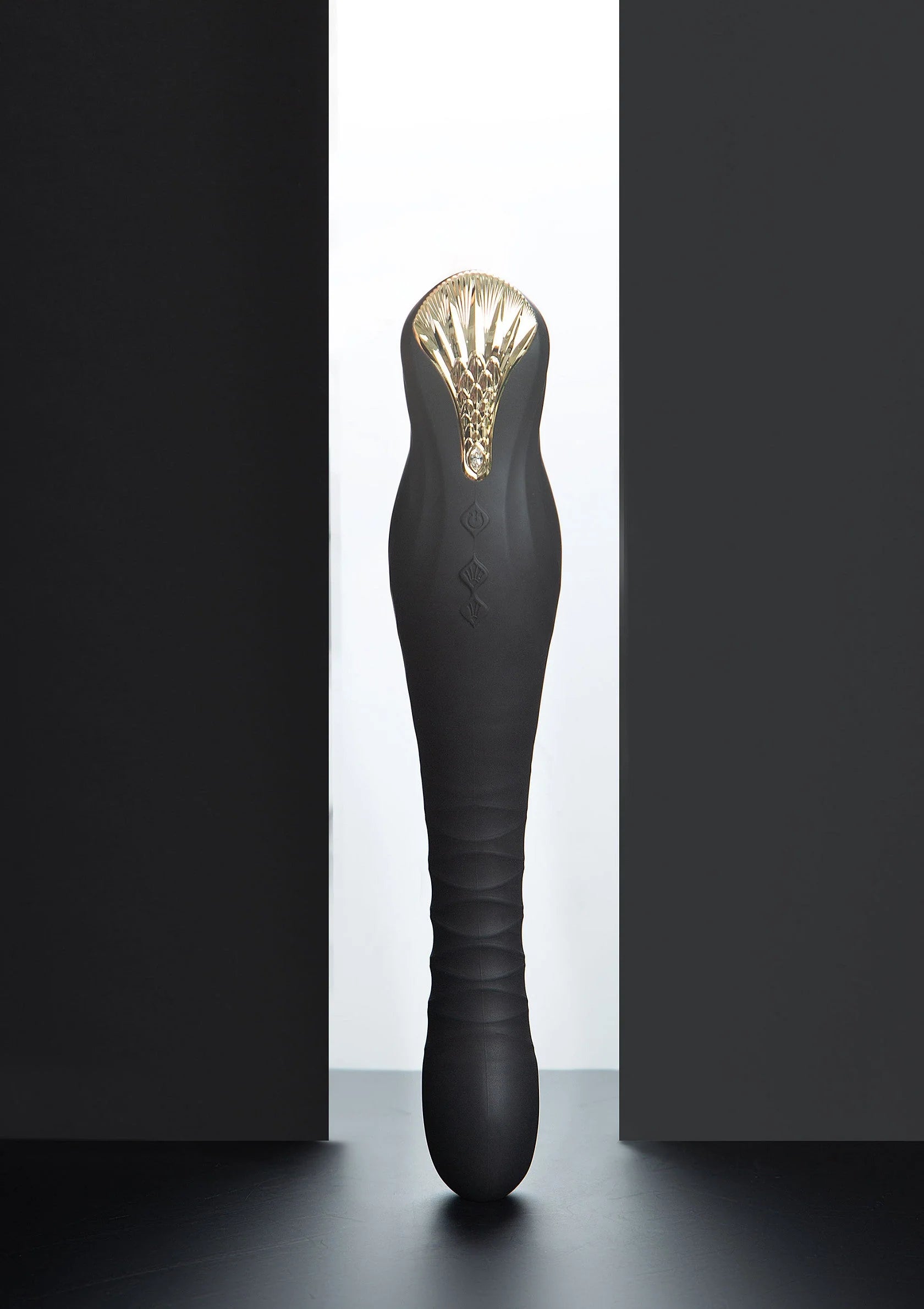 Zwarte dildo met goudkleurige kop en glanzende ribbels aan de bovenkant.