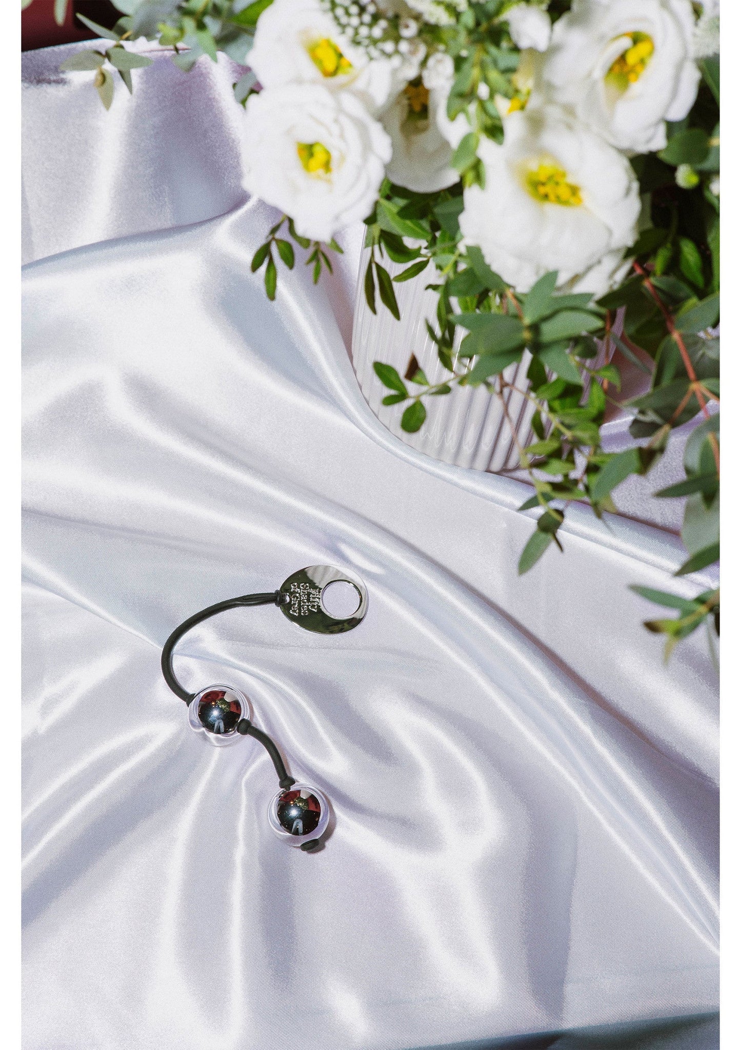 Zilverkleurige kogels met zwart koord op witte stof naast bloemen