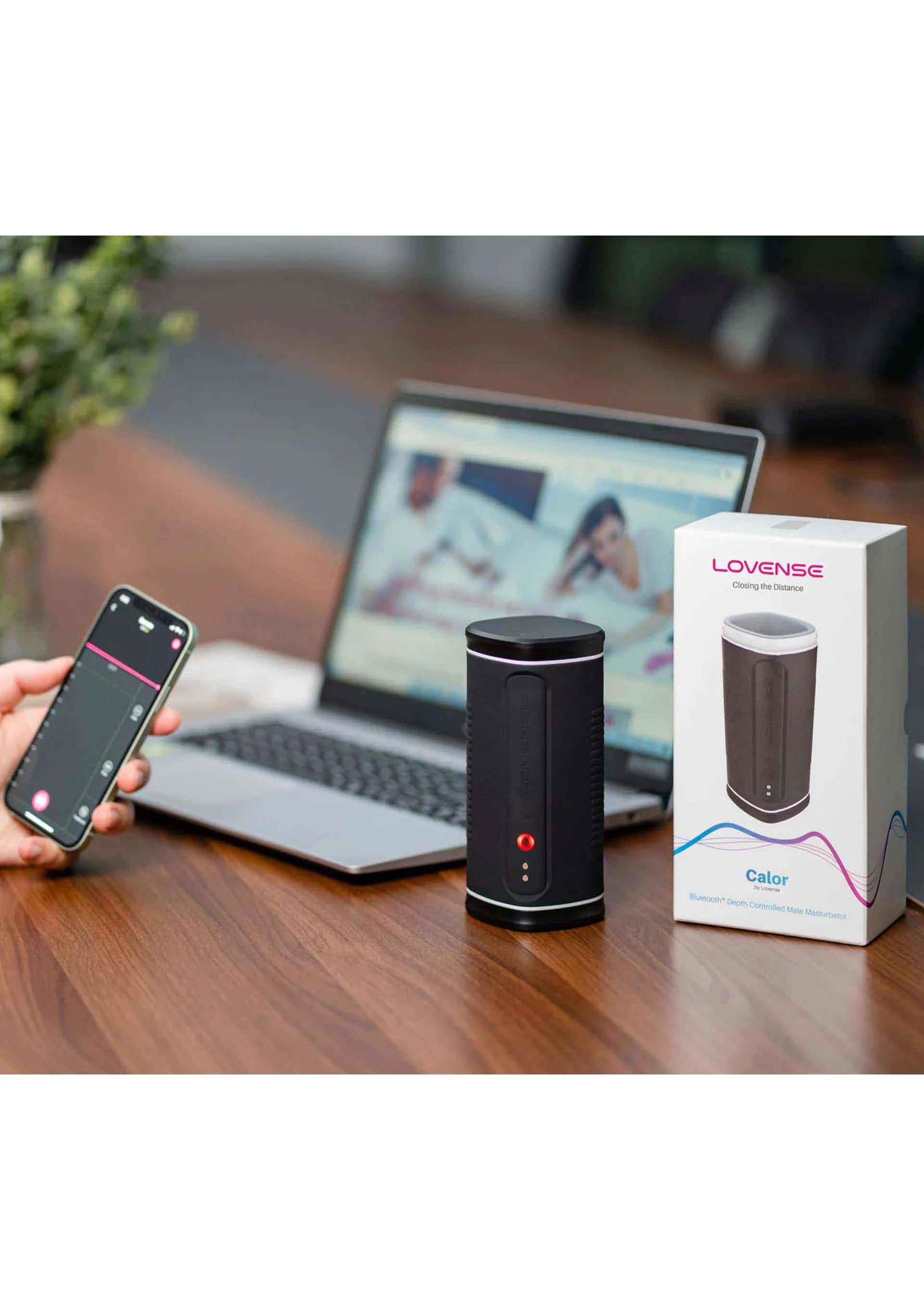 Zwarte Lovesense Calor masturbator op tafel met smartphone en laptop in beeld
