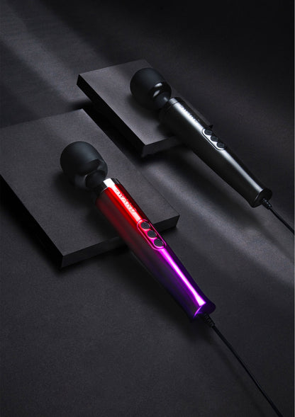 Vibrerende massager met ronde kop in rood en paars, kabel aangesloten naast een zwarte standaard.