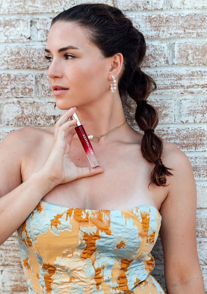 Vrouw met vlecht houdt rode parfumsprayfles bij haar kaak