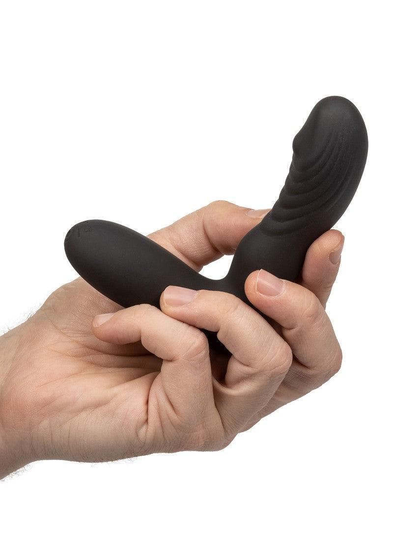 Hand holding black silicone anal vibrator with curved, textured design on white background